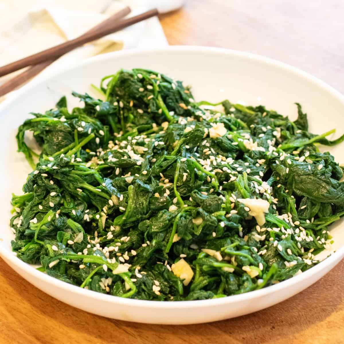 a bowl of blanched spinach with garlic and sesame seeds and chopsticks.