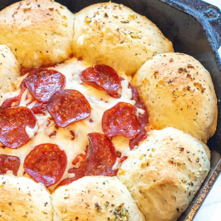 a cast iron skillet with baked rolls, and a cheesy dip with pepperoni in the center.