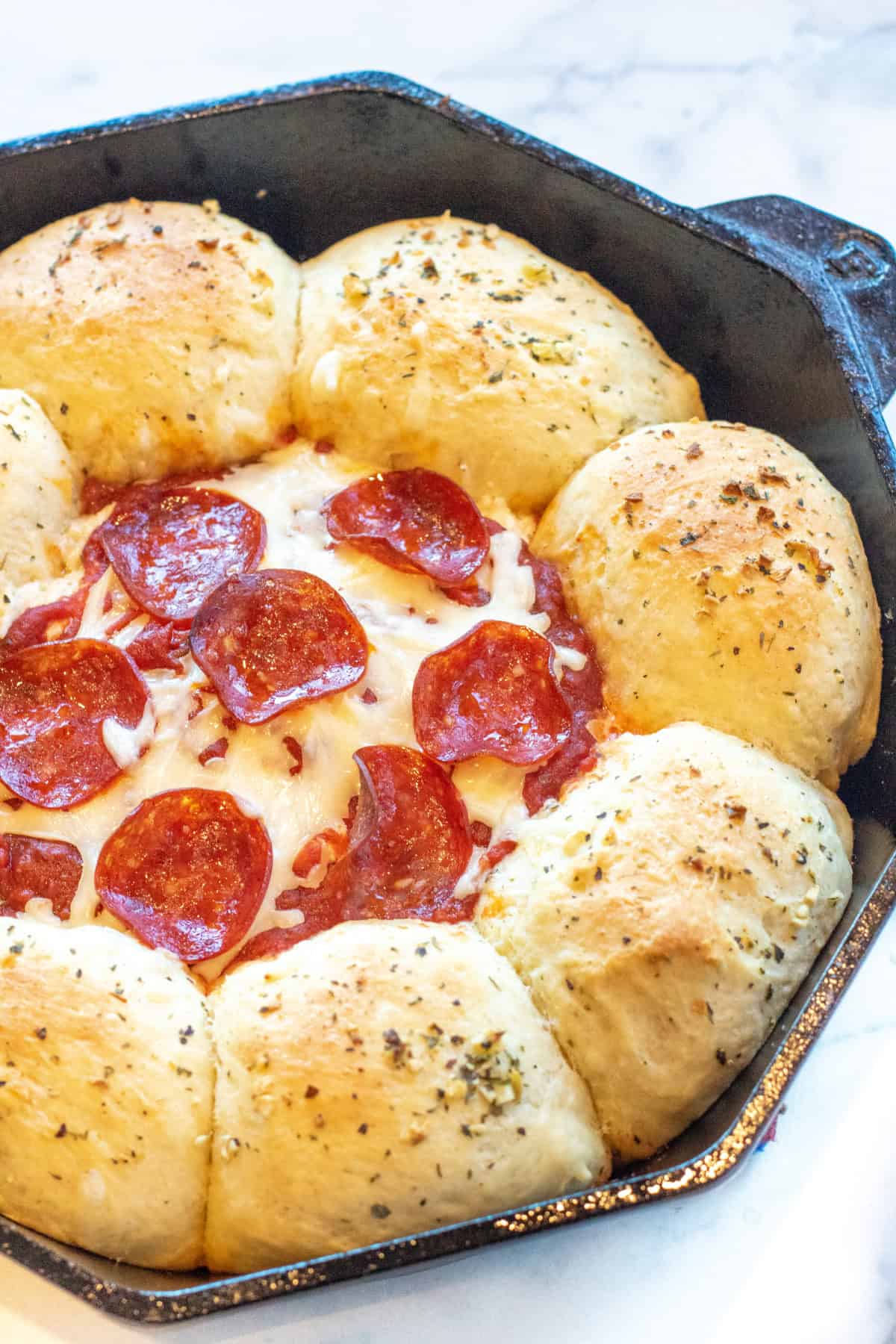 a cast iron skillet with baked rolls, and a cheesy dip with pepperoni in the center.