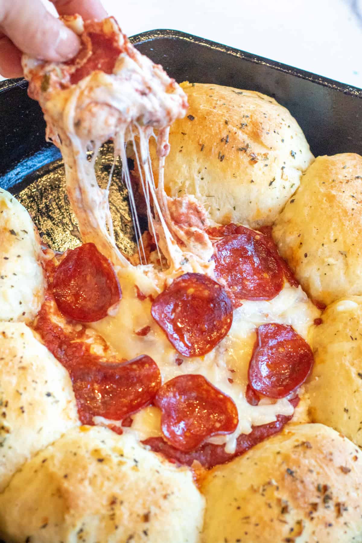 a hand pulling at a cheese dip with a piece of a roll with the dip surrounded by rolls.