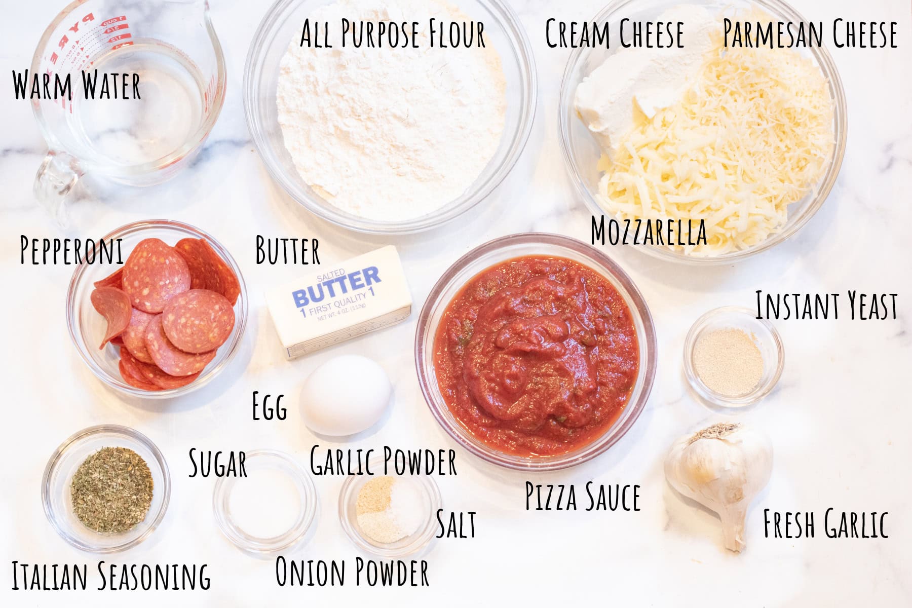 bowls of flour, pizza sauce, cheeses, pepperoni, garlic, Italian seasoning, sugar, egg, butter, and spices labeled. 
