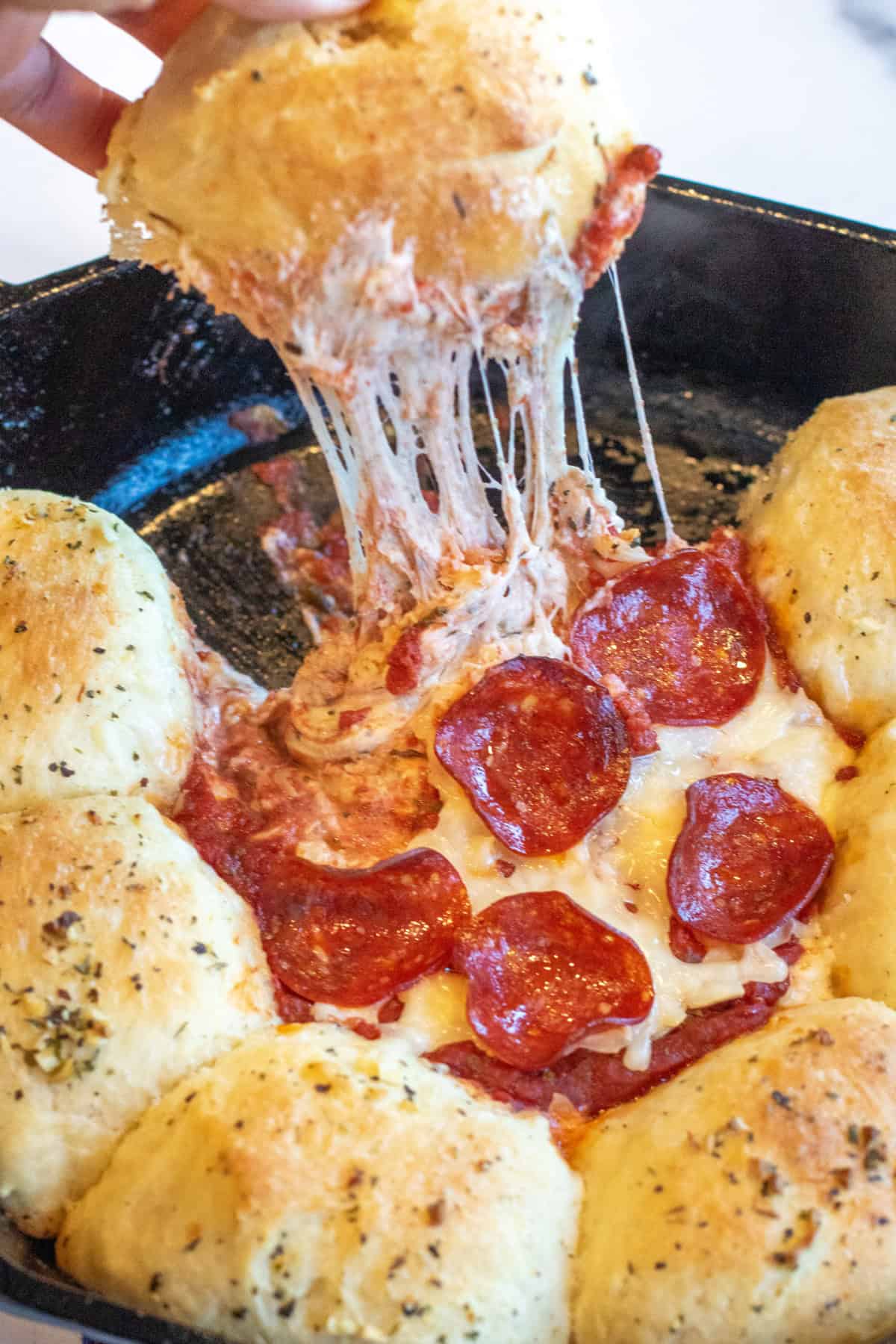 a roll being pulled out of a cast iron with a cheese pill from a pizza dip surrounded by rolls.