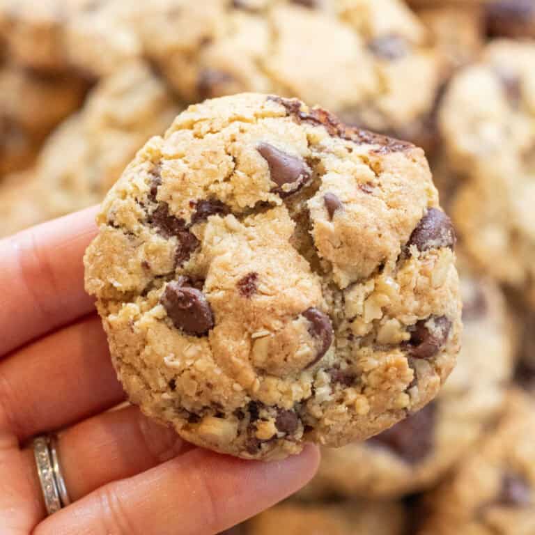 a hand holding a big chocolate chip cookie over a tray of cookies.