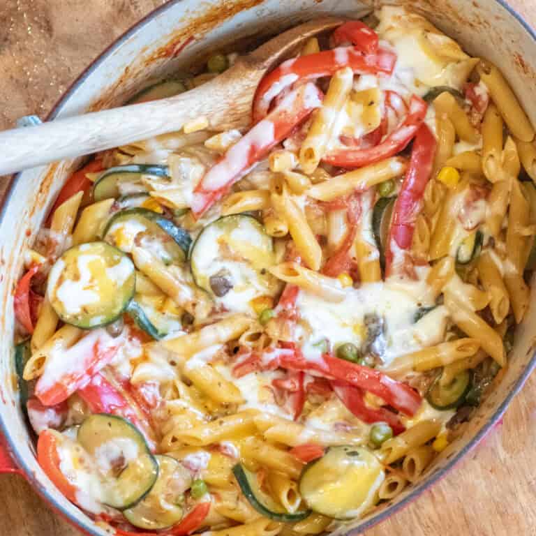 an overhead of cheesy pasta with veggies with a wooden spoon in it.