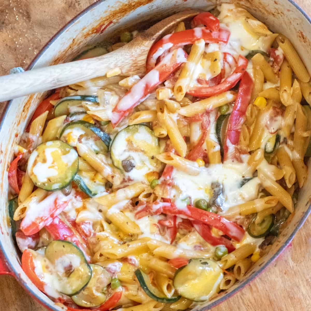 an overhead of cheesy pasta with veggies with a wooden spoon in it.