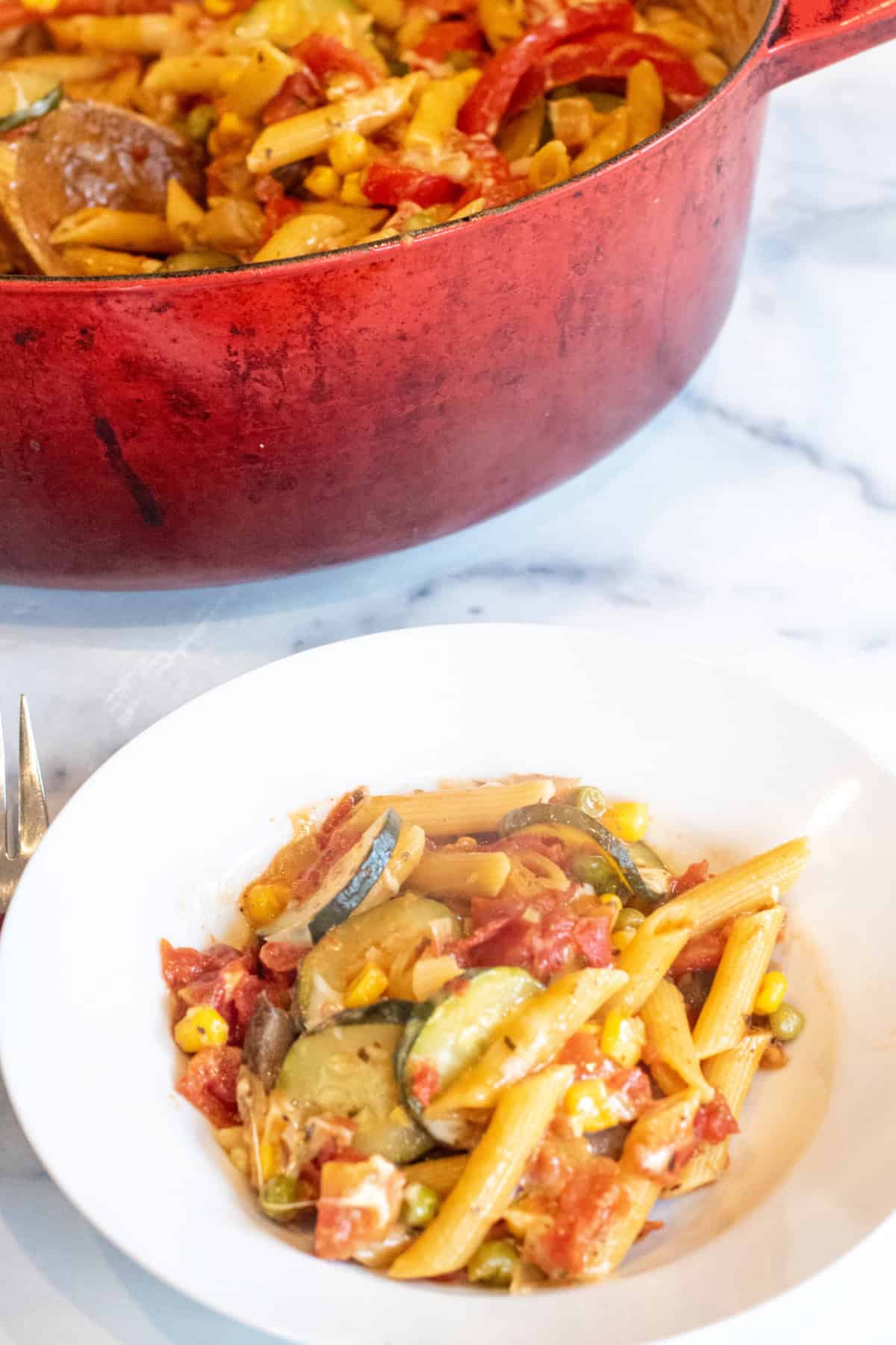 a bowl of pasta with veggies in front of a dutch oven.
