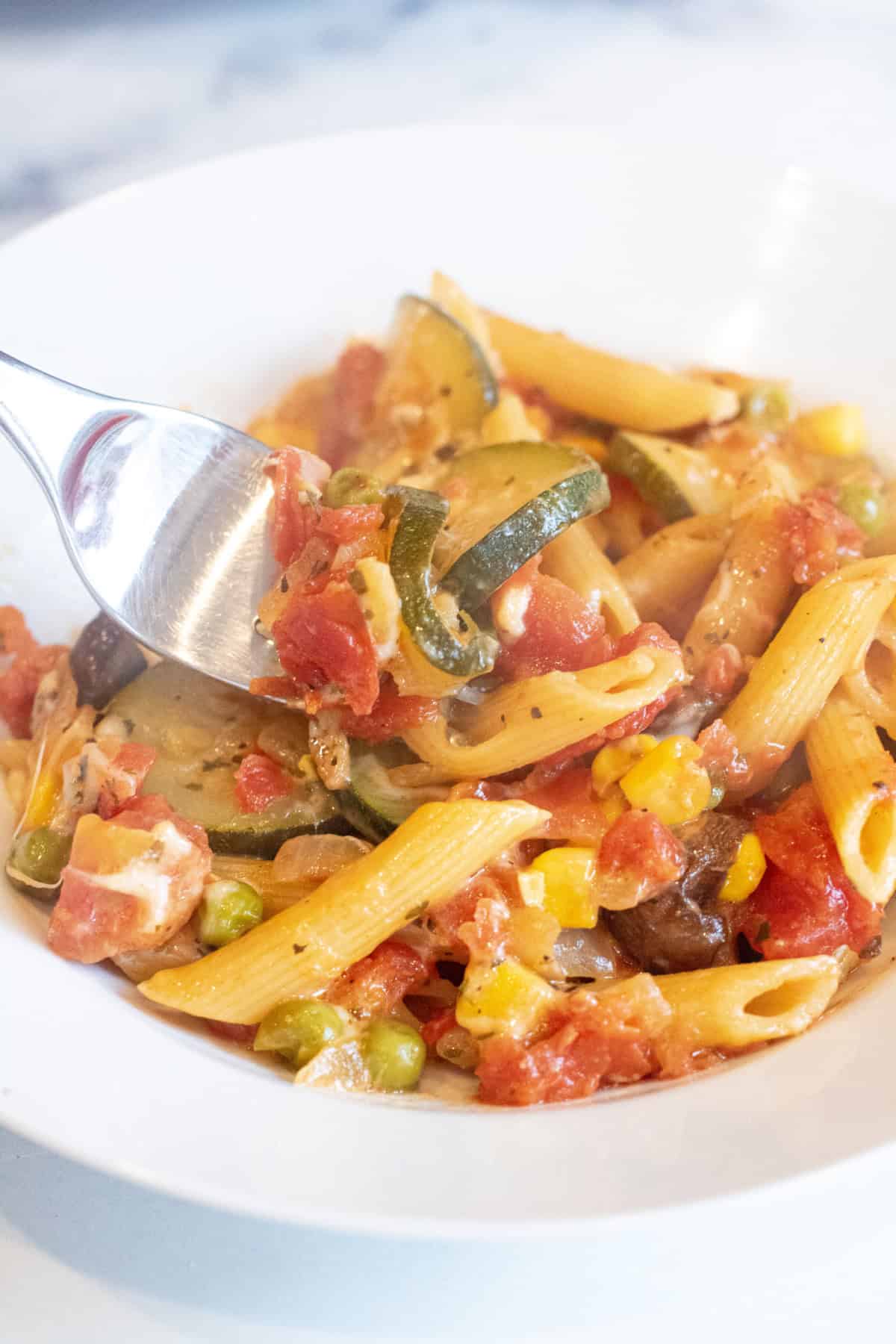 a bowl of cooked pasta and veggies with a forkful. 