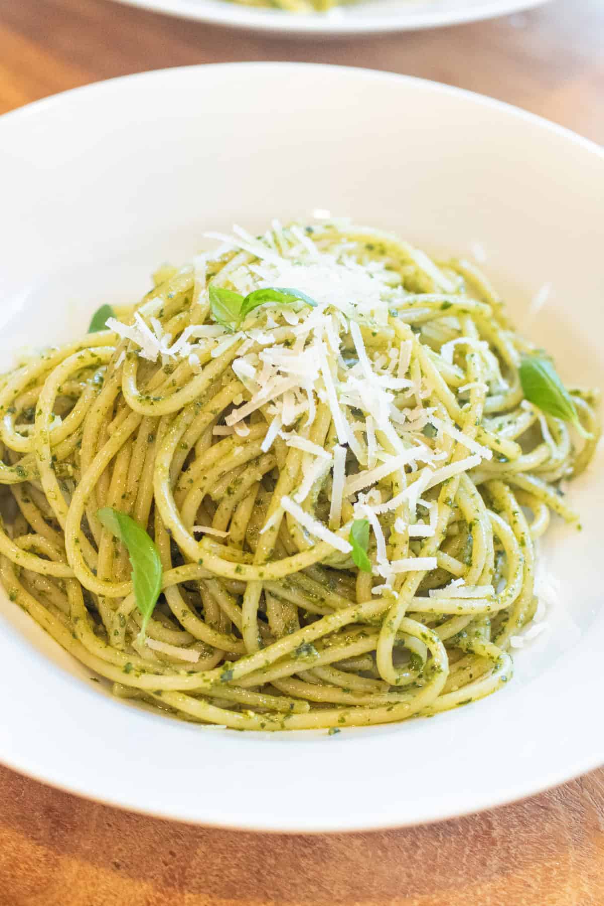 a bowl of spaghetti with pesto topped with Parmesan cheese and basil.