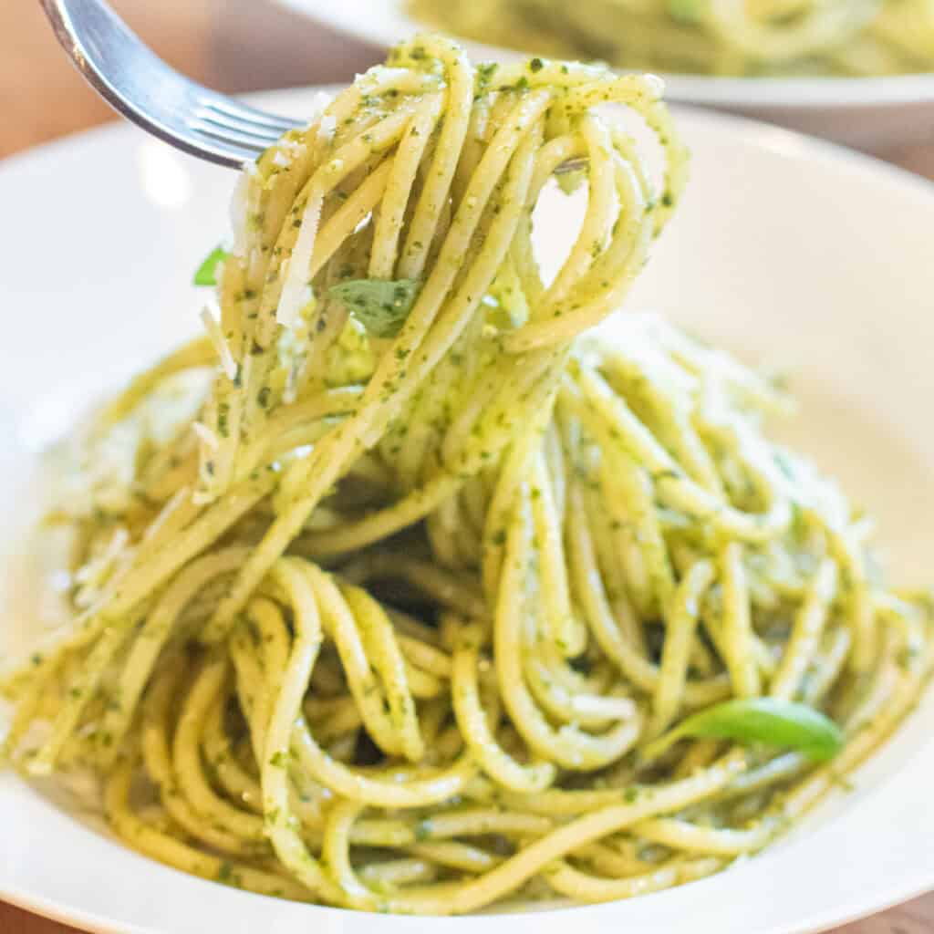 a bowl of pesto pasta with a fork holding some up.
