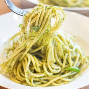 a bowl of pesto pasta with a fork holding some up.