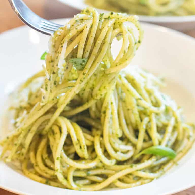 a bowl of pesto pasta with a fork holding some up.
