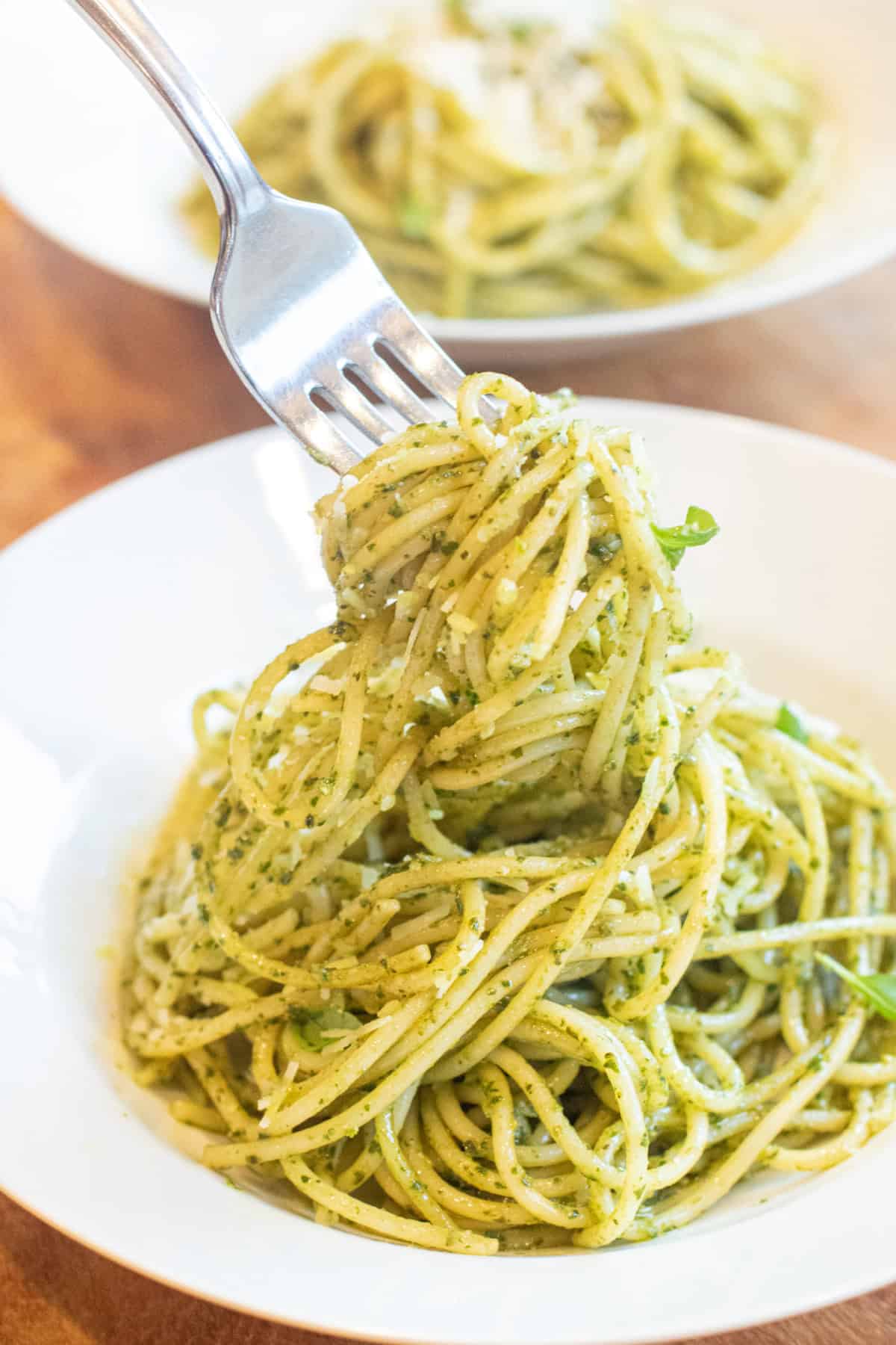 a bowl of pesto pasta with a fork holding some up.
