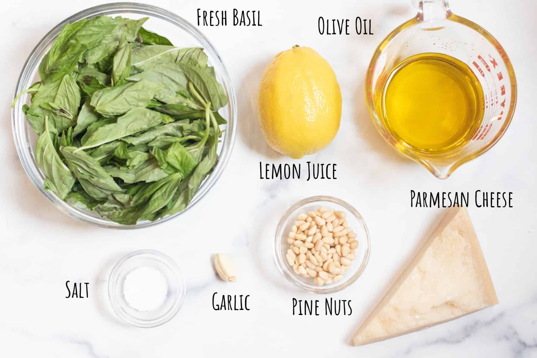 a bowl of fresh basil, lemon, oil, pine nuts, parmesan cheese, and salt all labeled.