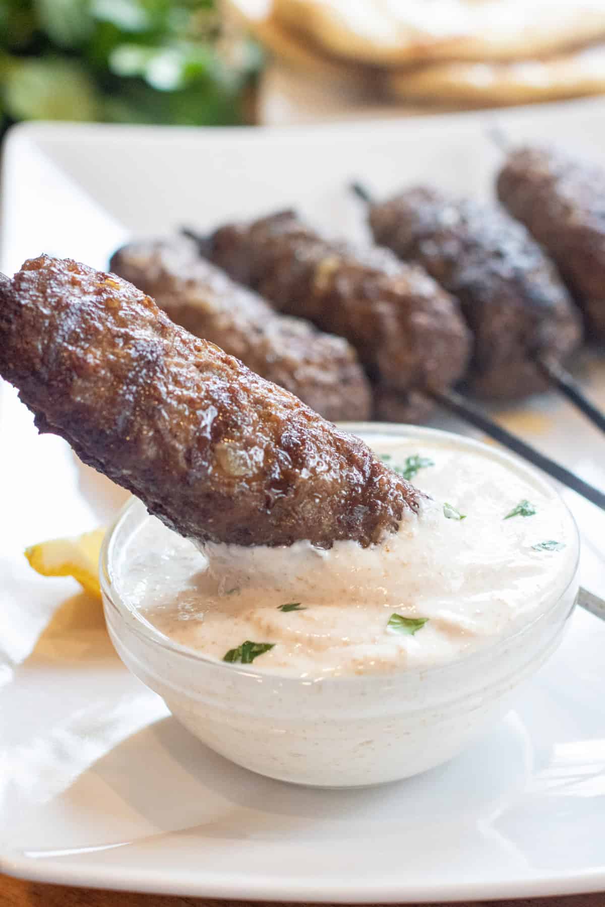 a grilled lamb kofta kebab being dipped into a yogurt sauce.