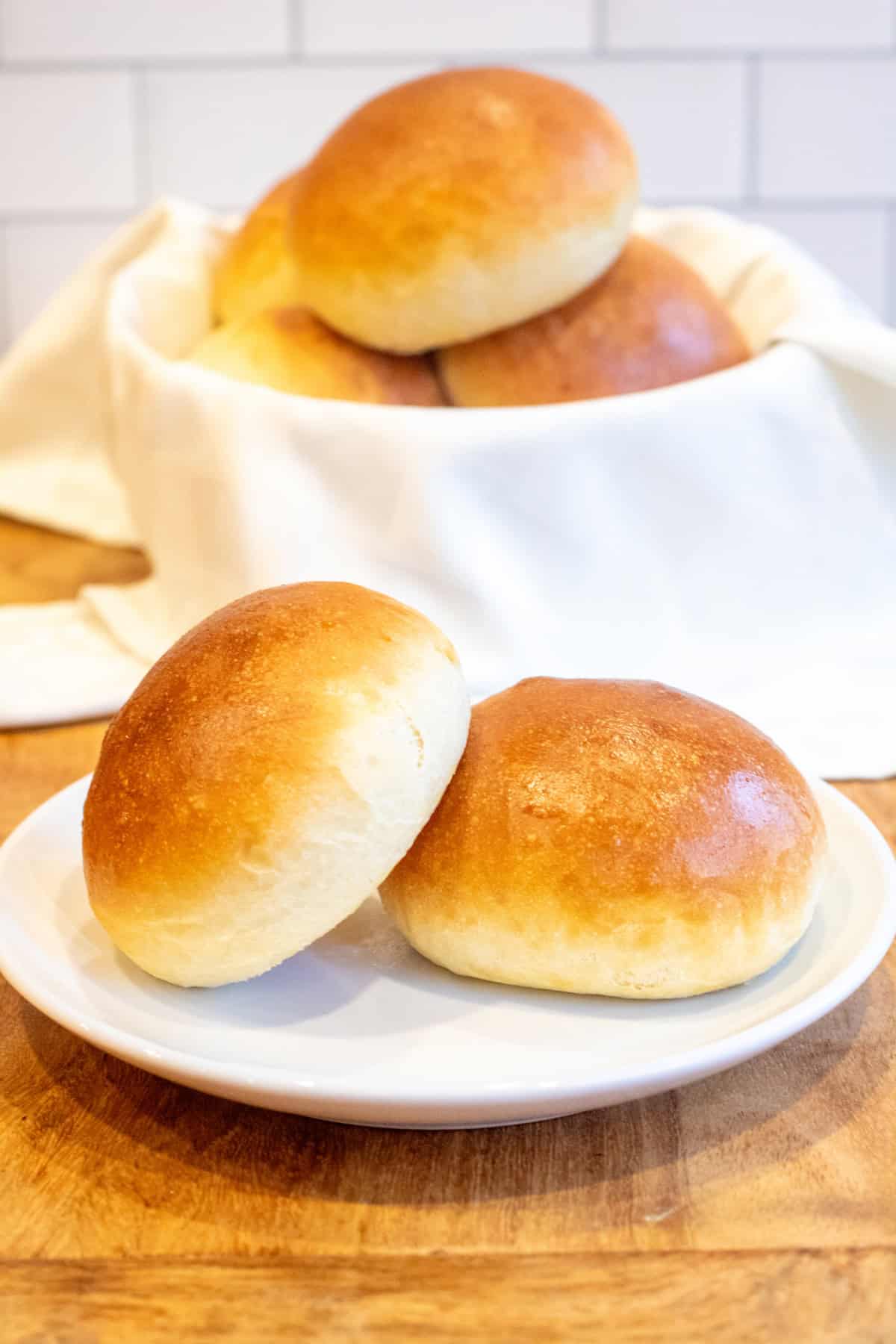 a plate with two brioche buns on it in front of a basket of buns.