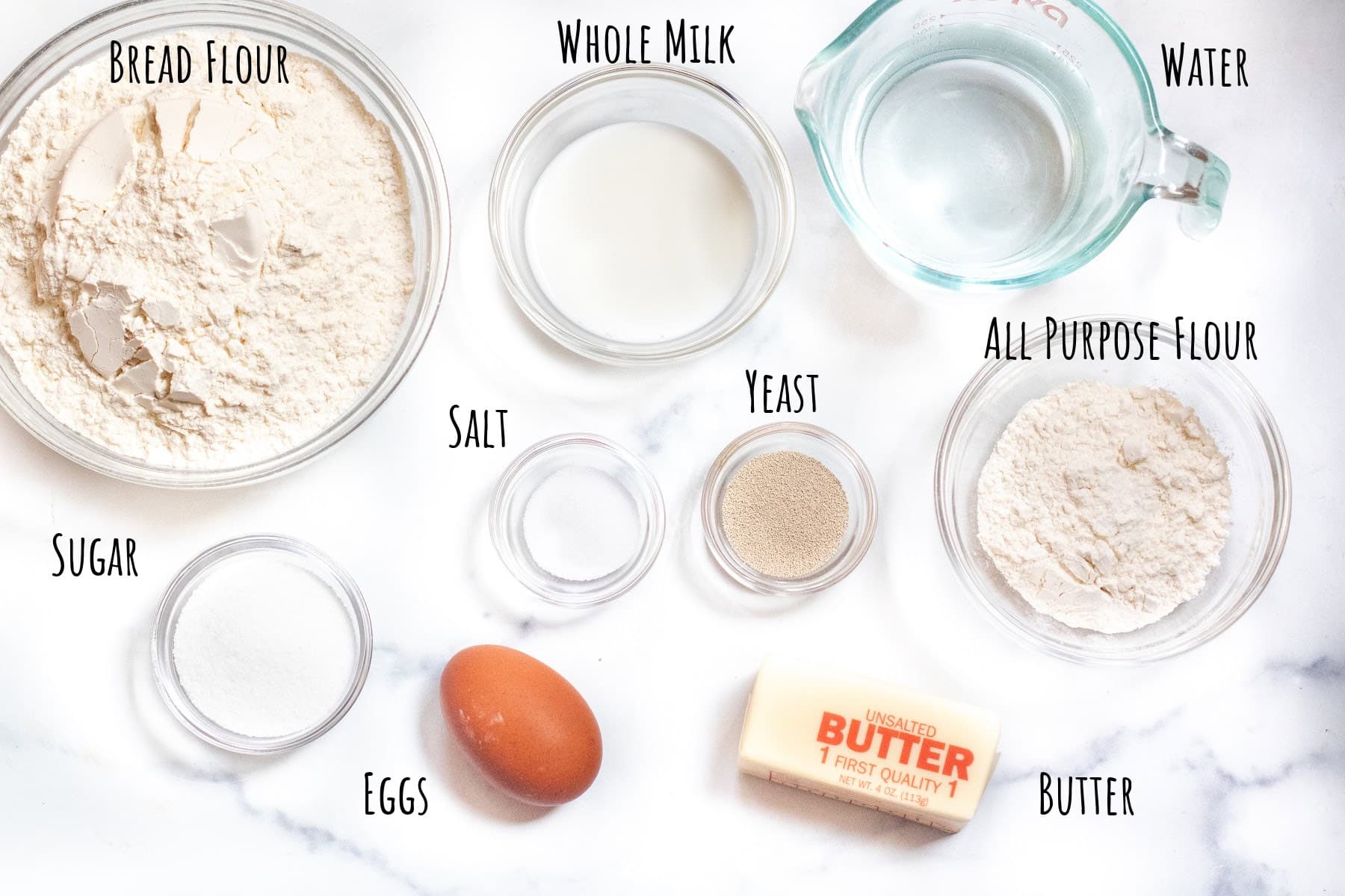 bowls of flours, milk, water, salt, sugar, yeast, an egg, and butter labeled.