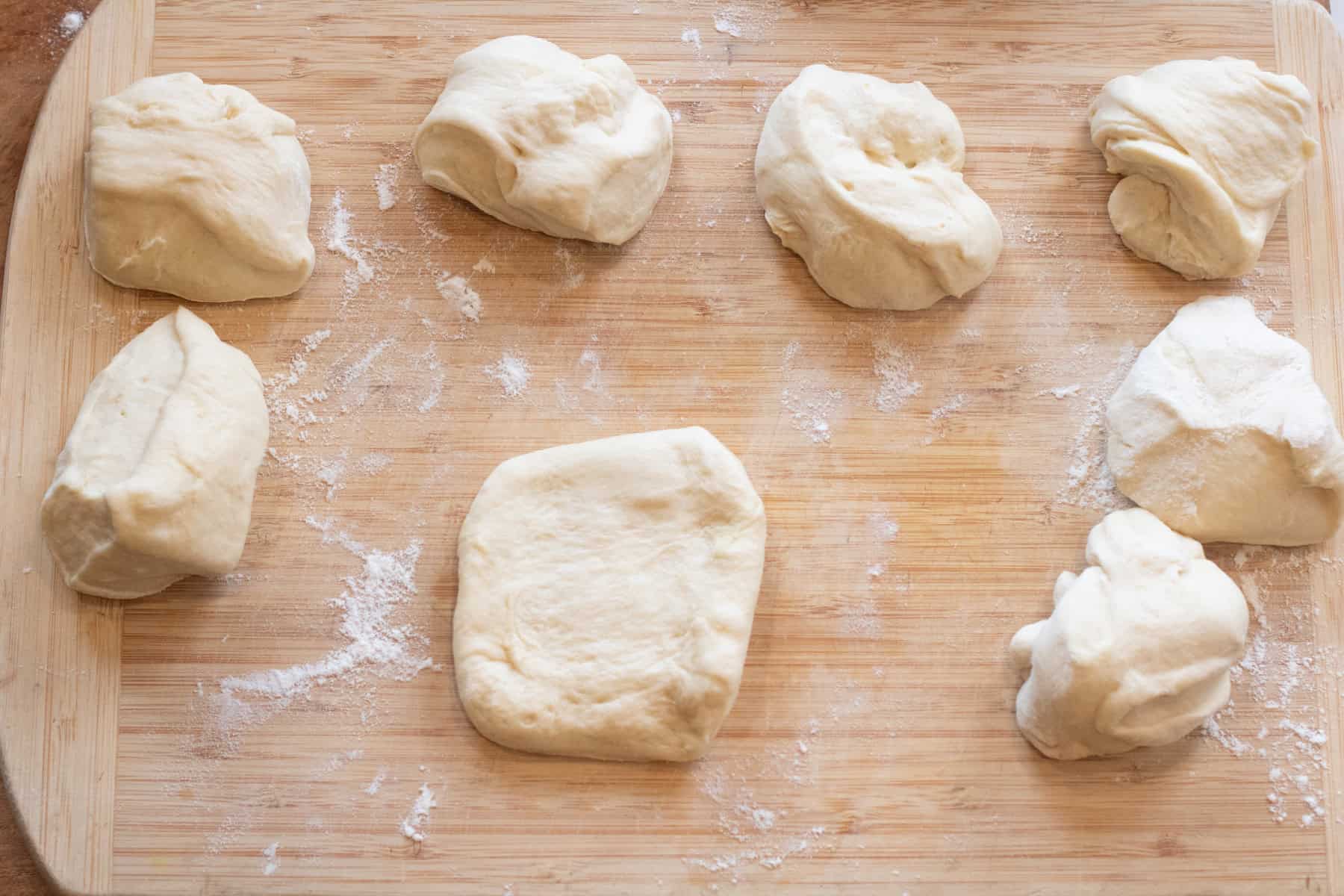 8 pieces of dough on a floured cutting board. 