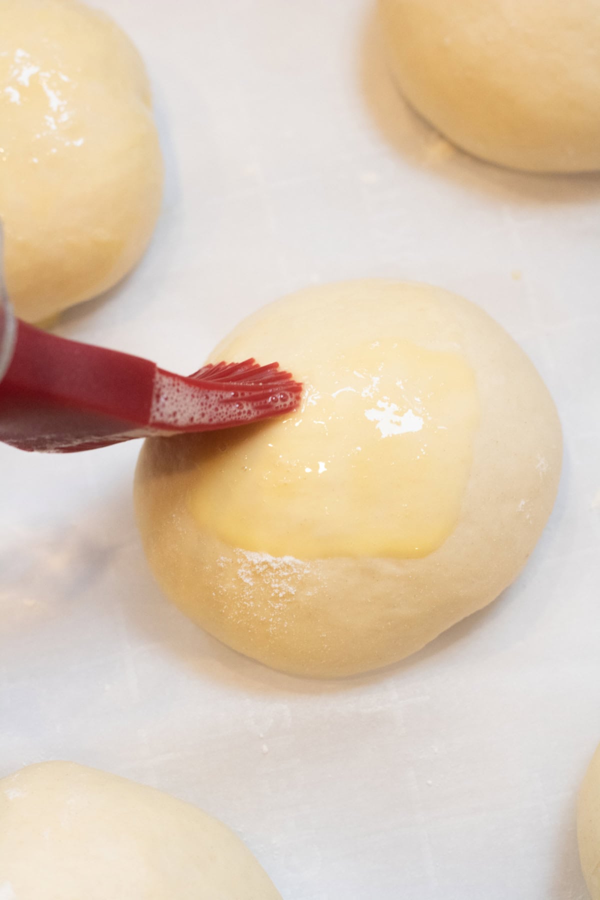 a brush giving a dough ball an egg wash. 