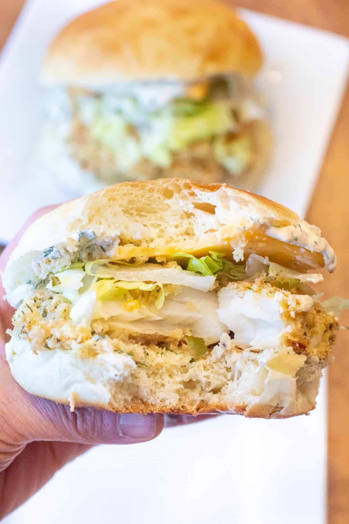 a hand holding a big fish sandwich with a bite taken out of it.