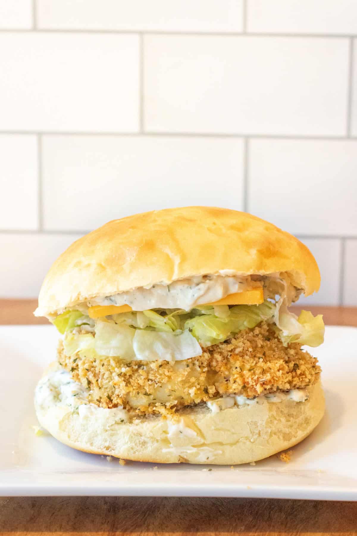 a breaded fish sandwich with lettuce and cheese on a brioche bun.