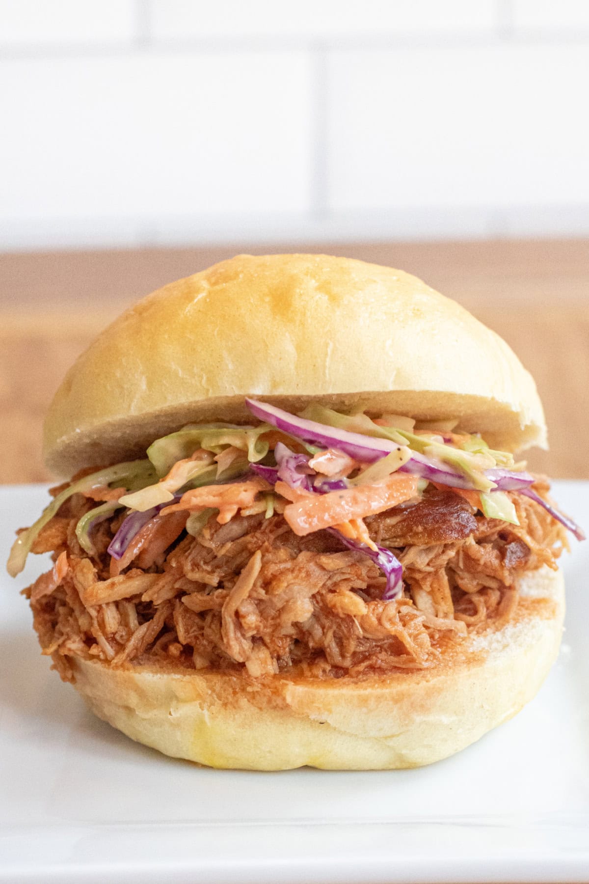 a close up of a pulled pork sandwich on a brioche bun on a plate with coleslaw.