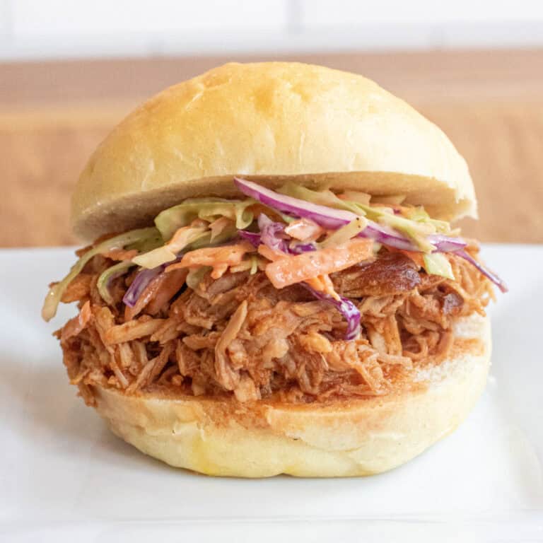 a close up of a pulled pork sandwich on a brioche bun on a plate with coleslaw.