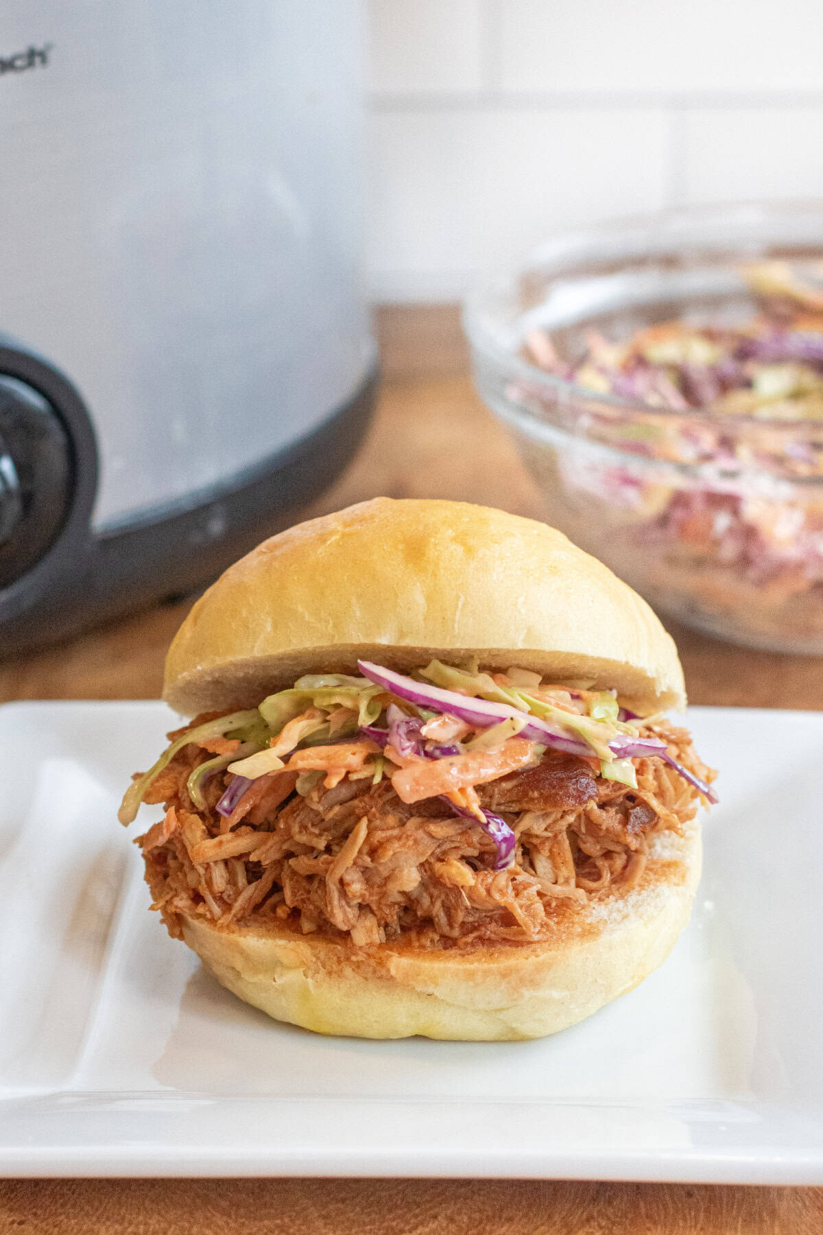 a close up of a pulled pork sandwich on a brioche bun on a plate with coleslaw.