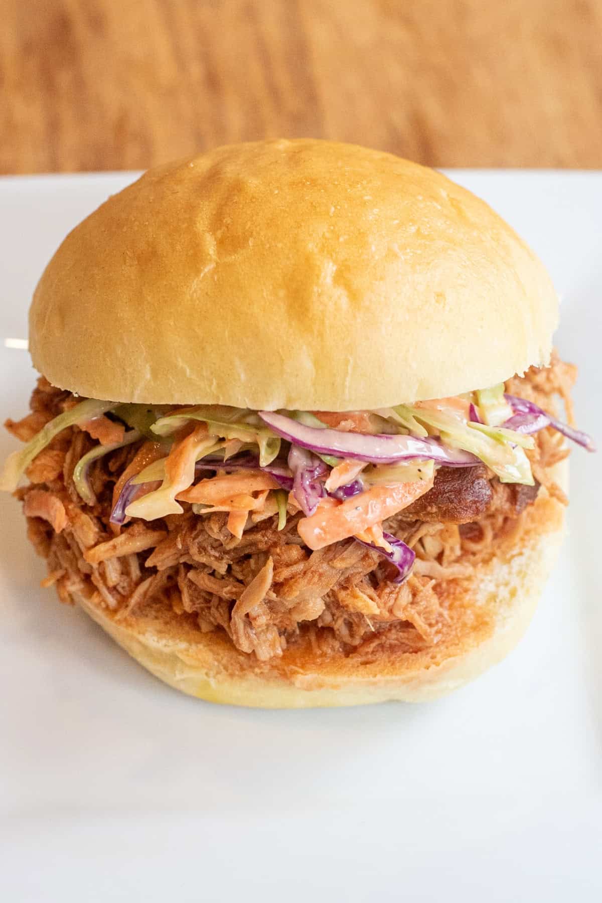 a close up of a pulled pork sandwich on a brioche bun on a plate with coleslaw.