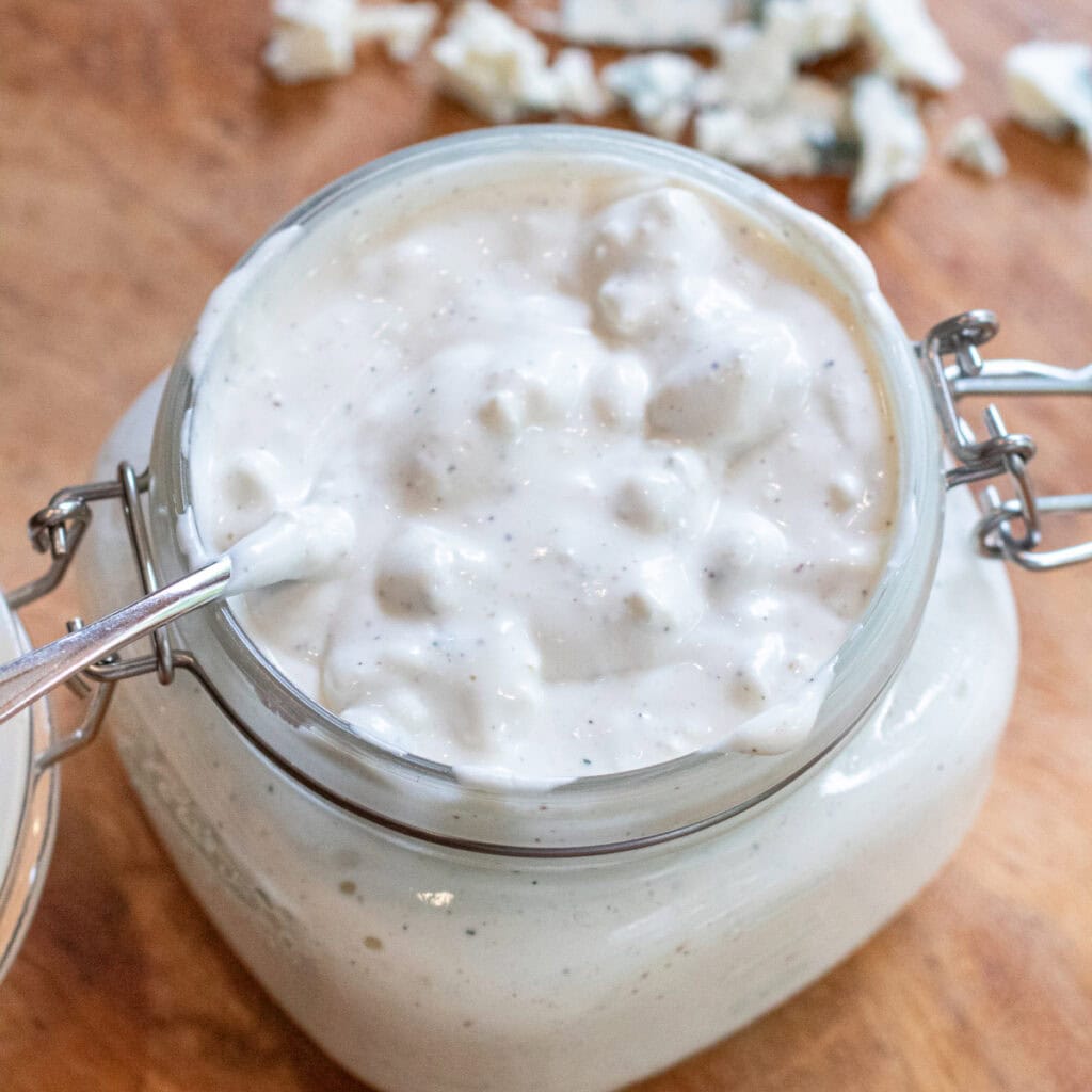 an overhead of an open mason jar of creamy chunky blue cheese dressing with a spoon in it.