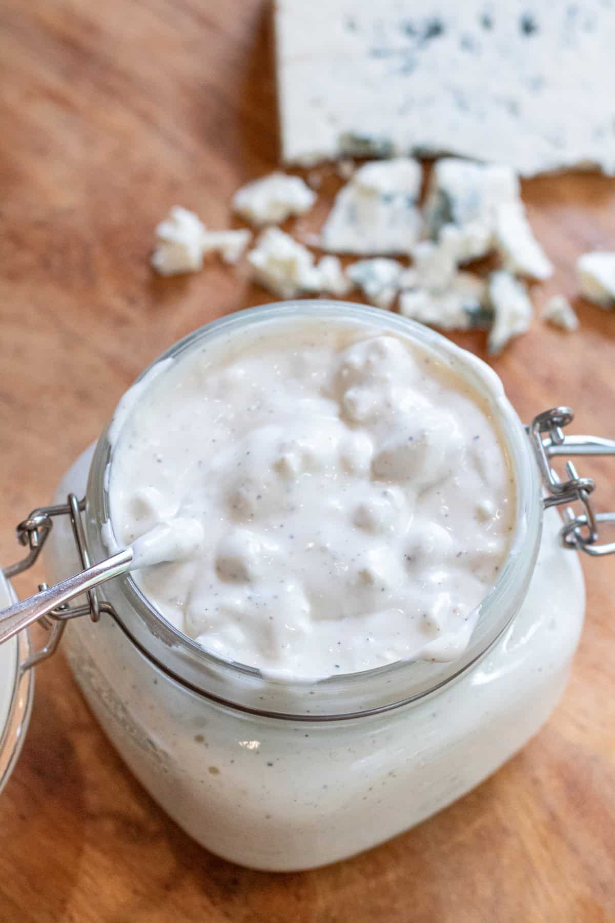 an overhead of an open mason jar of creamy chunky blue cheese dressing with a spoon in it.