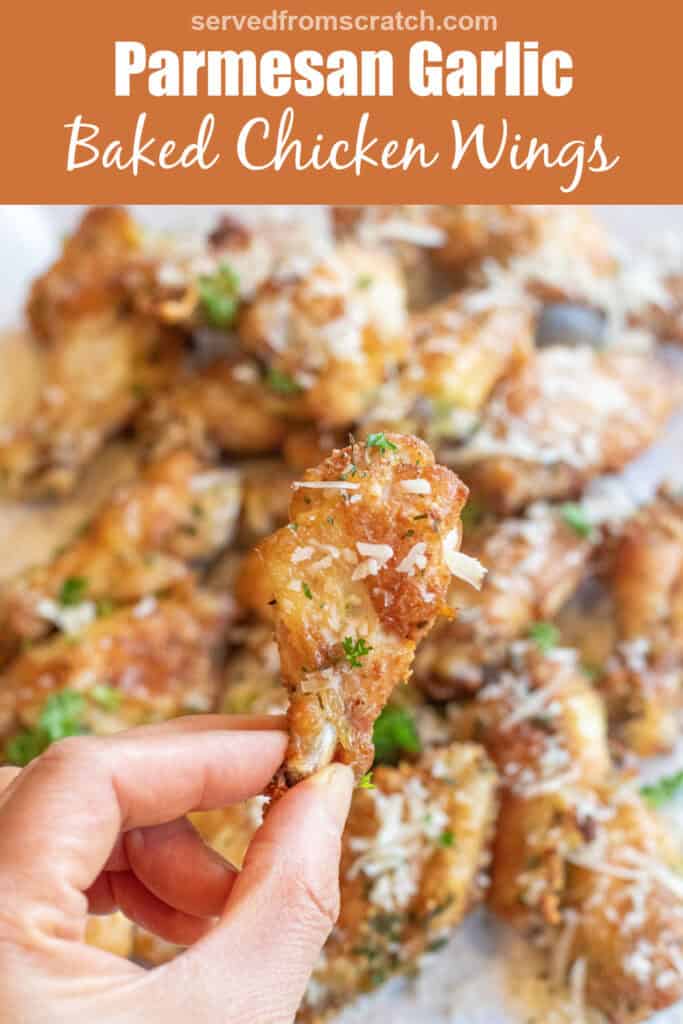 a hand holding a crispy chicken wing over a plate of chicken wings coated with Parmesan cheese with Pinterest pin text.