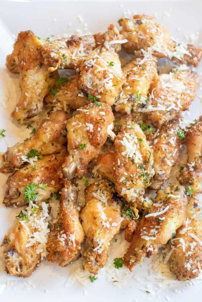 a plate of crispy chicken wings with parmesan cheese and parsley.