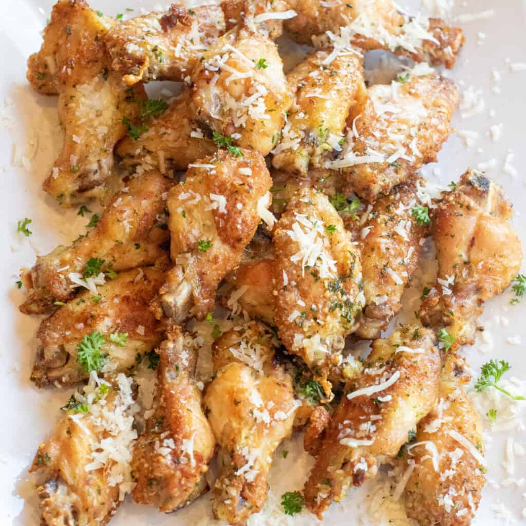 a plate of baked chicken wings with parsley and parmesan sprinkled on top.