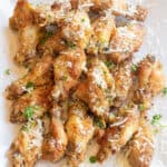 a plate of baked chicken wings with parsley and parmesan sprinkled on top.