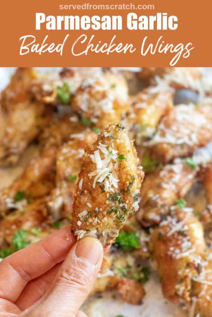 a hand holding a crispy chicken wing over a plate of chicken wings coated with Parmesan cheese with Pinterest pin text.