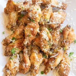 a plate of baked chicken wings with parsley and parmesan sprinkled on top.