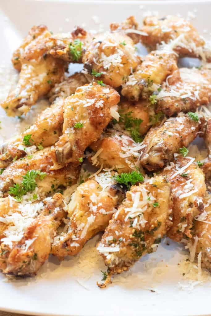 a plate of baked chicken wings with parsley and parmesan sprinkled on top.
