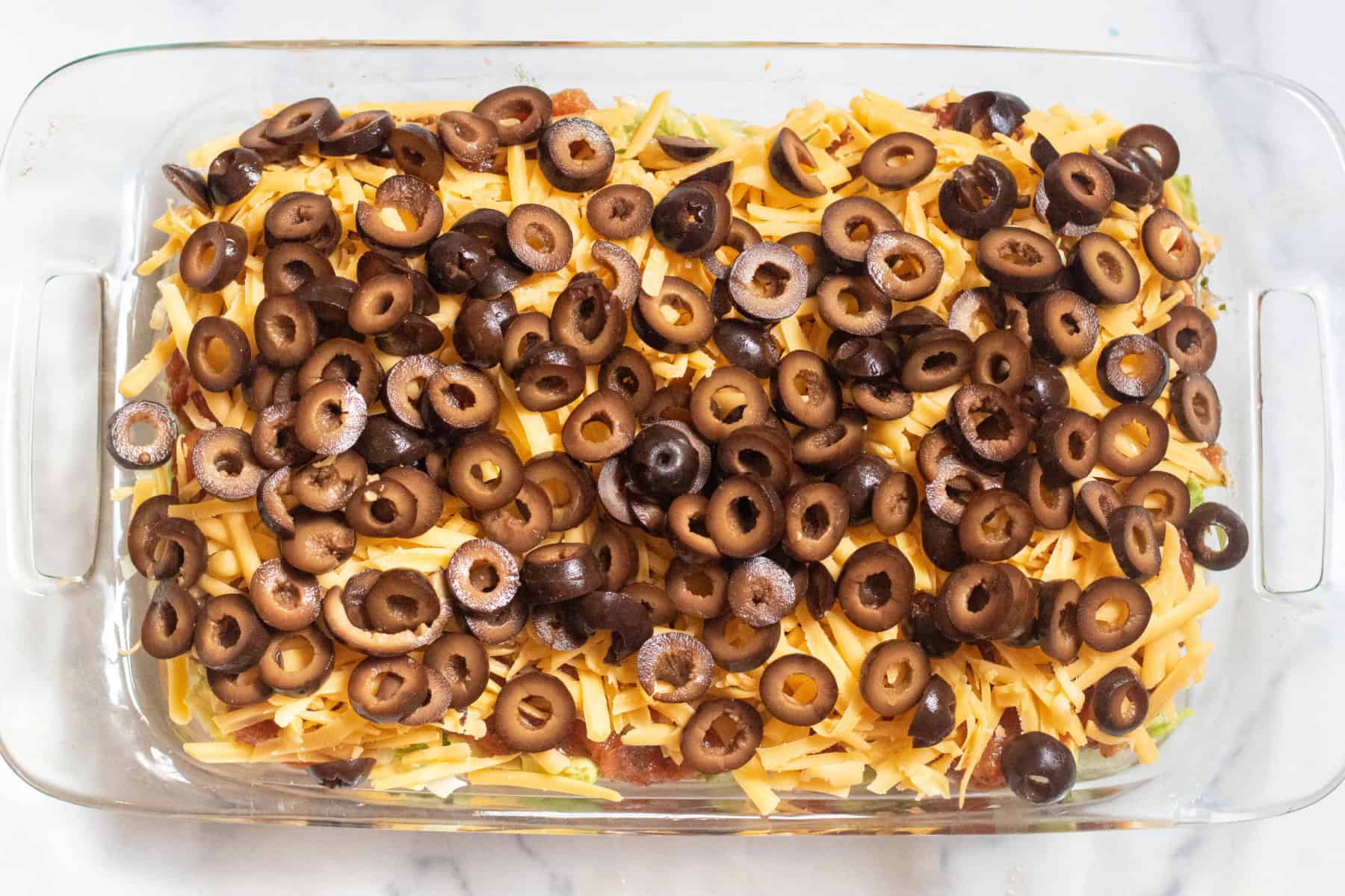 a baking tray with shredded cheese and sliced olives on top.