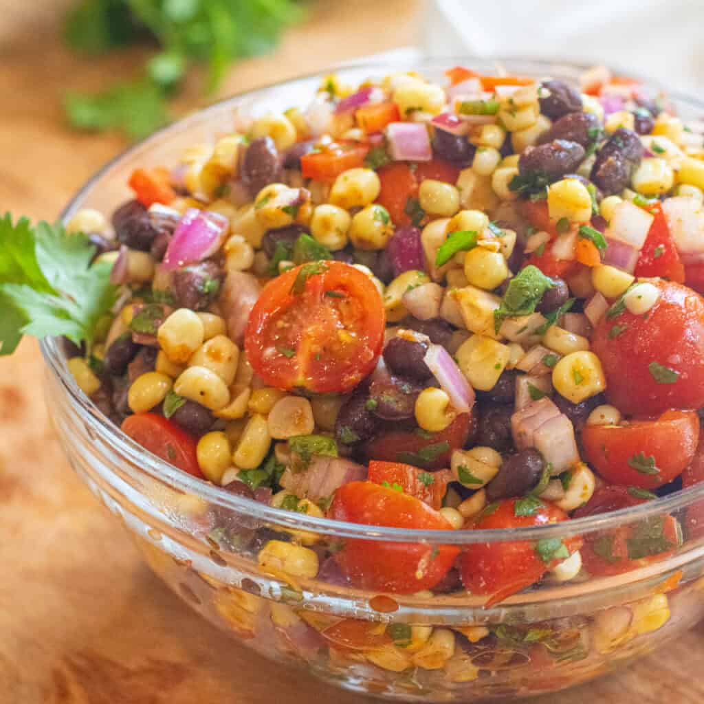 a large bowl of a corn and black bean salad with halved tomatoes and herbs.