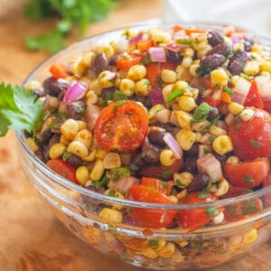 a large bowl of a corn and black bean salad with halved tomatoes and herbs.