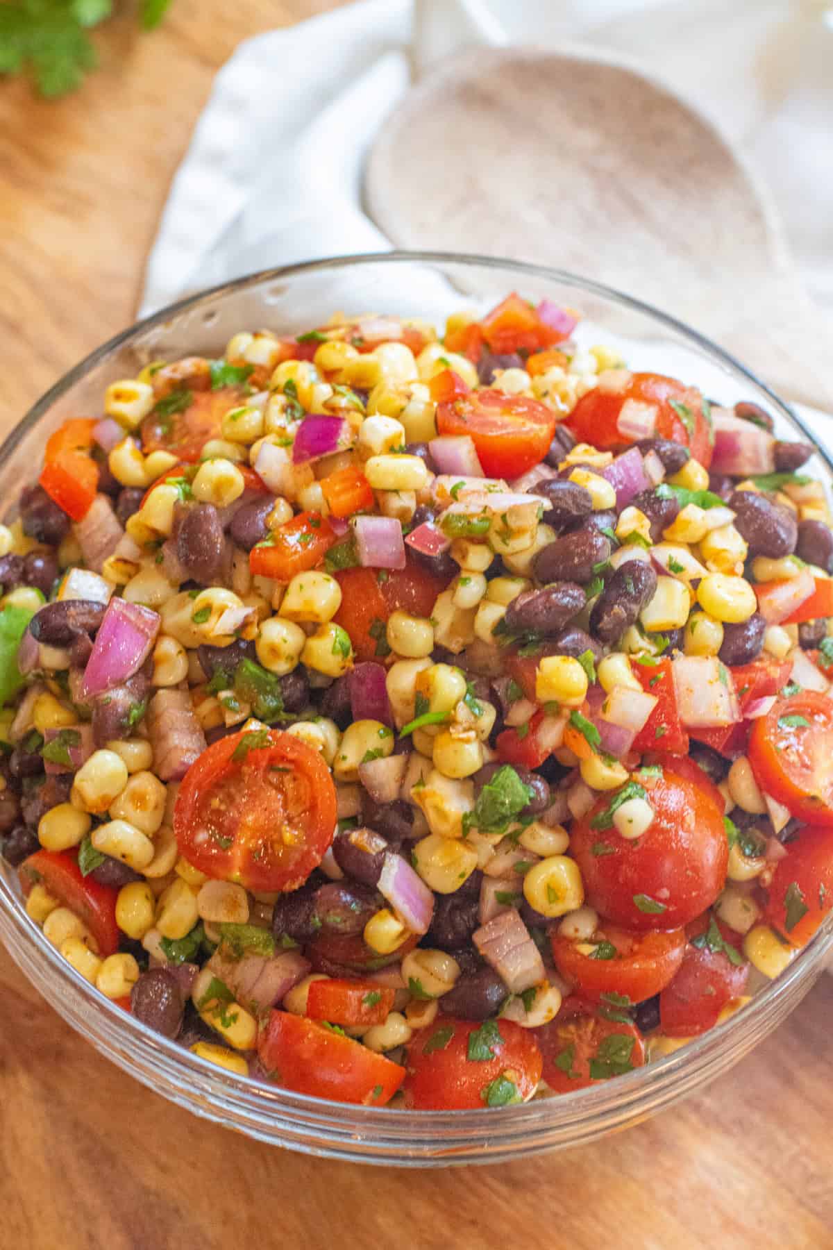 a large bowl of a corn and black bean salad with halved tomatoes and herbs.