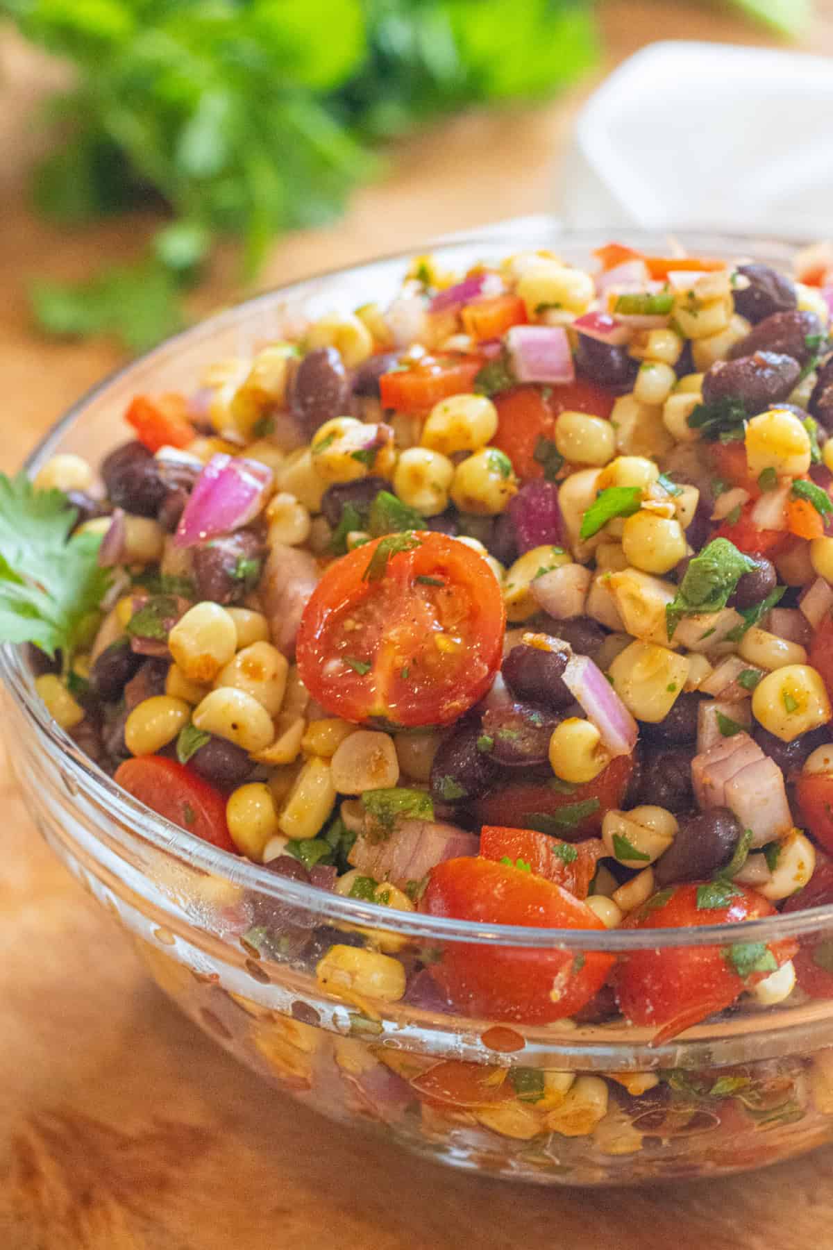 a large bowl of a corn and black bean salad with halved tomatoes and herbs.