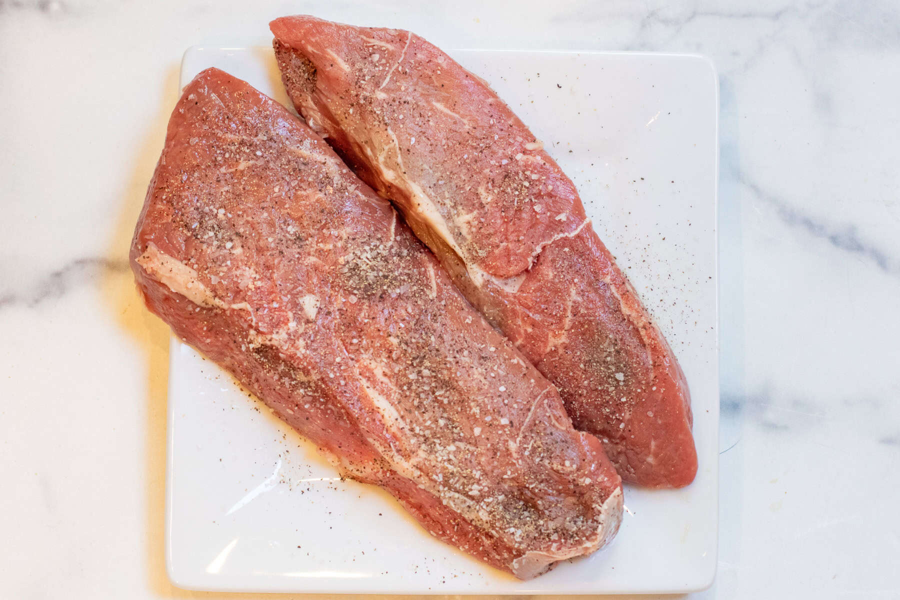 raw steaks seasoned with salt and pepper.
