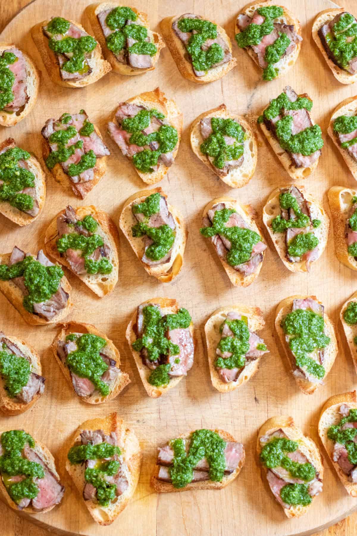 an overhead of a cutting board of chimichurri topped steak crostini.