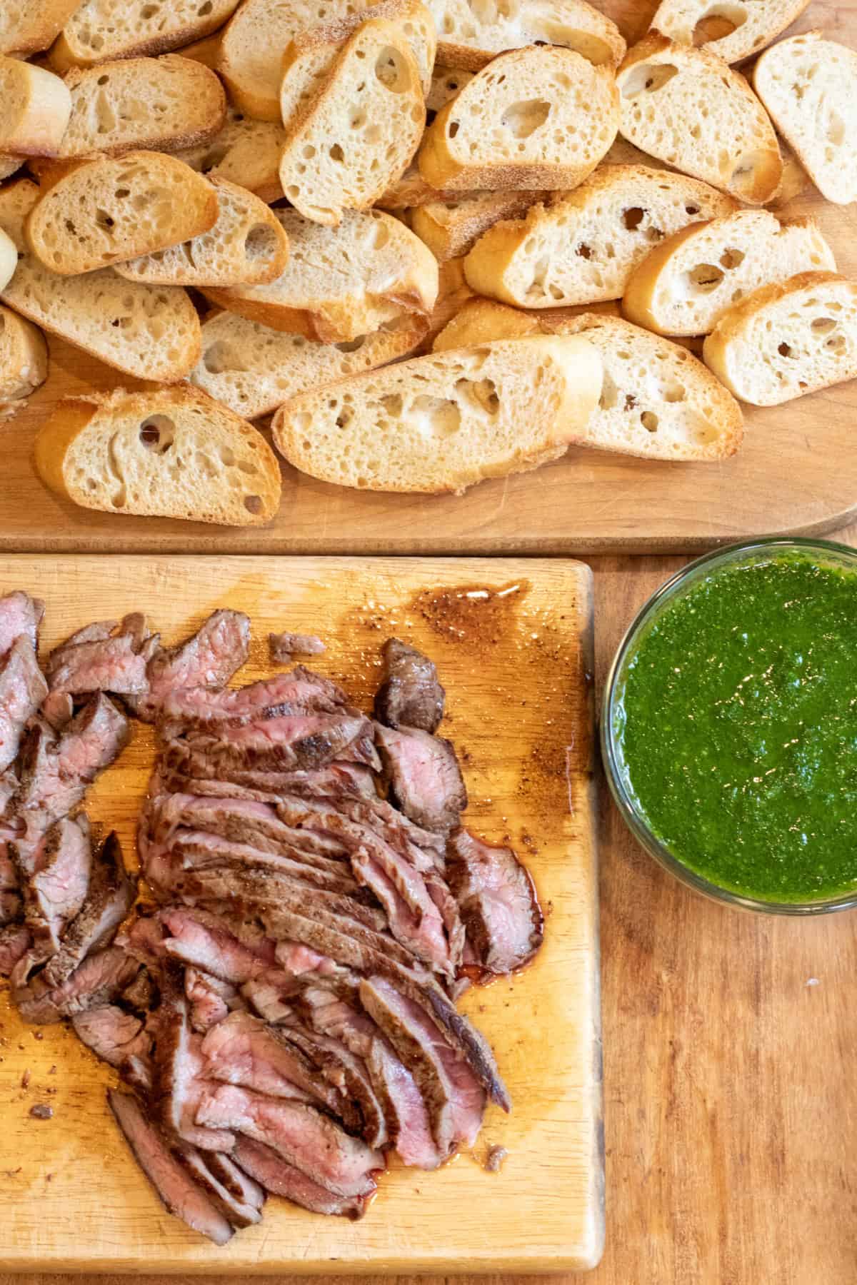 sliced steak, a bowl of chimichurri, and a board of sliced and toasted baguette.