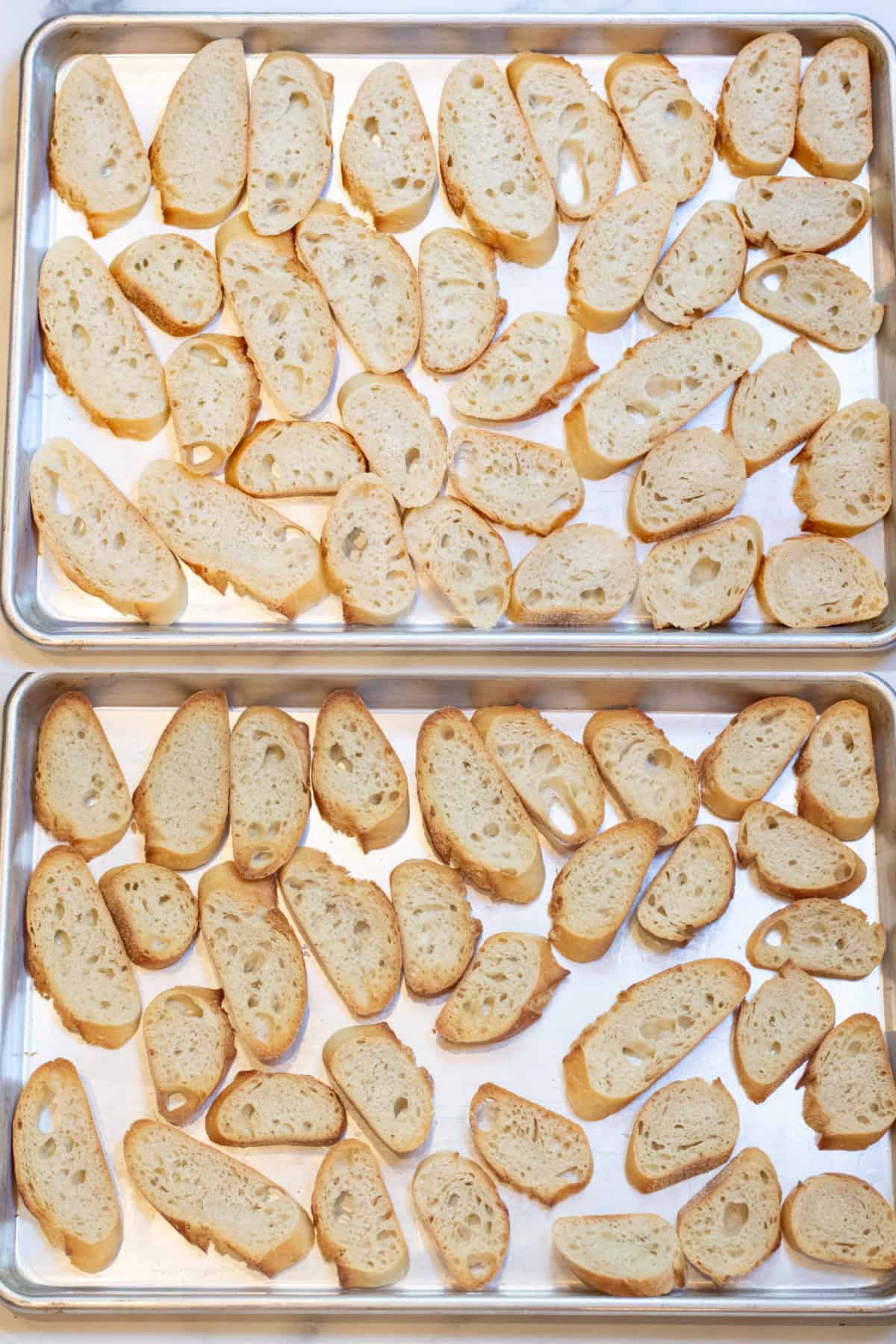 two trays of sliced baguettes, one raw and one of them toasted.
