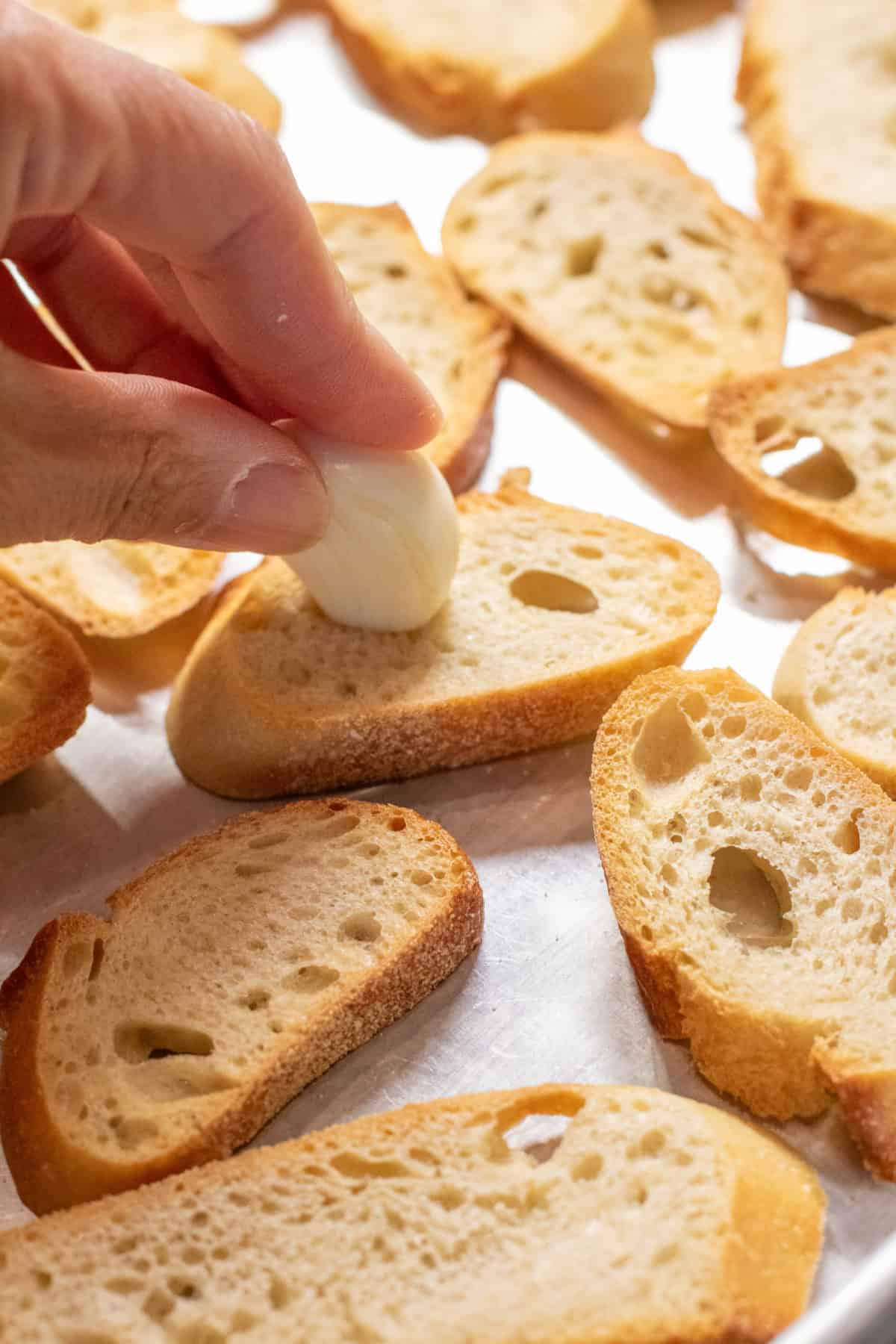 a hand holding a slice of garlic on a baguette slice.