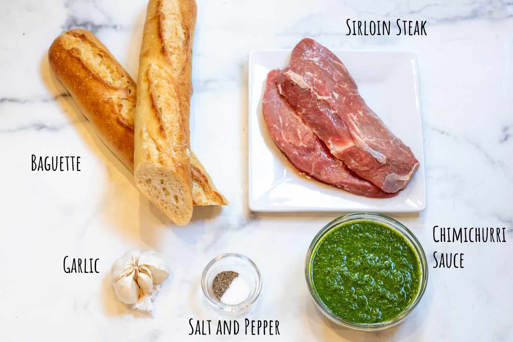 a baguette, bowl of chimichurri, raw steaks, salt and pepper, and garlic labeled.