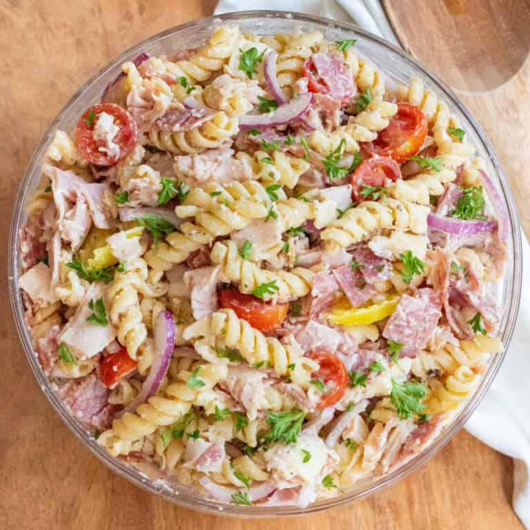 an overhead of a pasta salad with meats, cheese, tomatoes, parsley, and banana peppers.