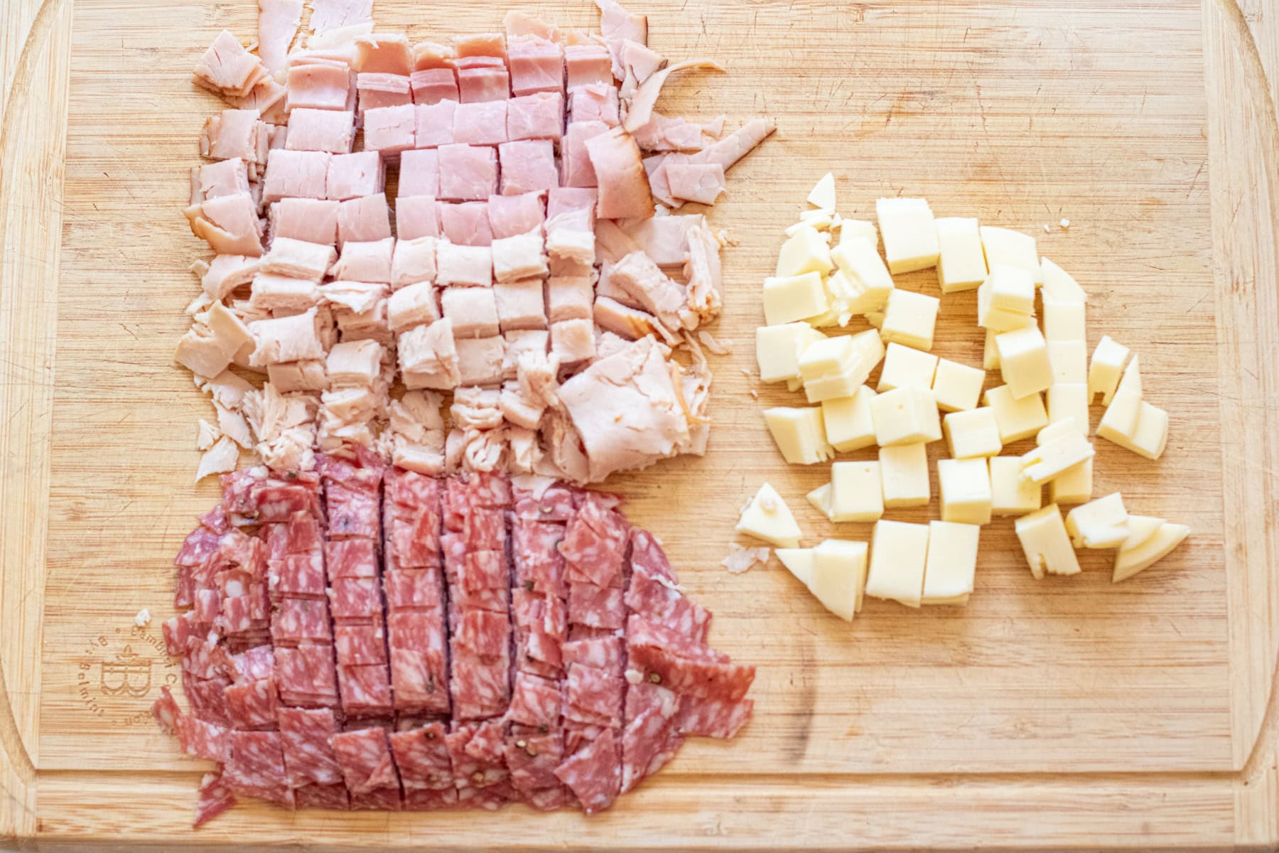 diced deli meats, salami, and cheese on a cutting board.